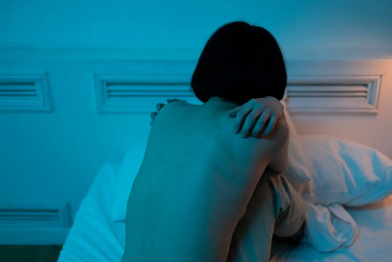 femme triste de dos assis et recroquevillée sur son lit