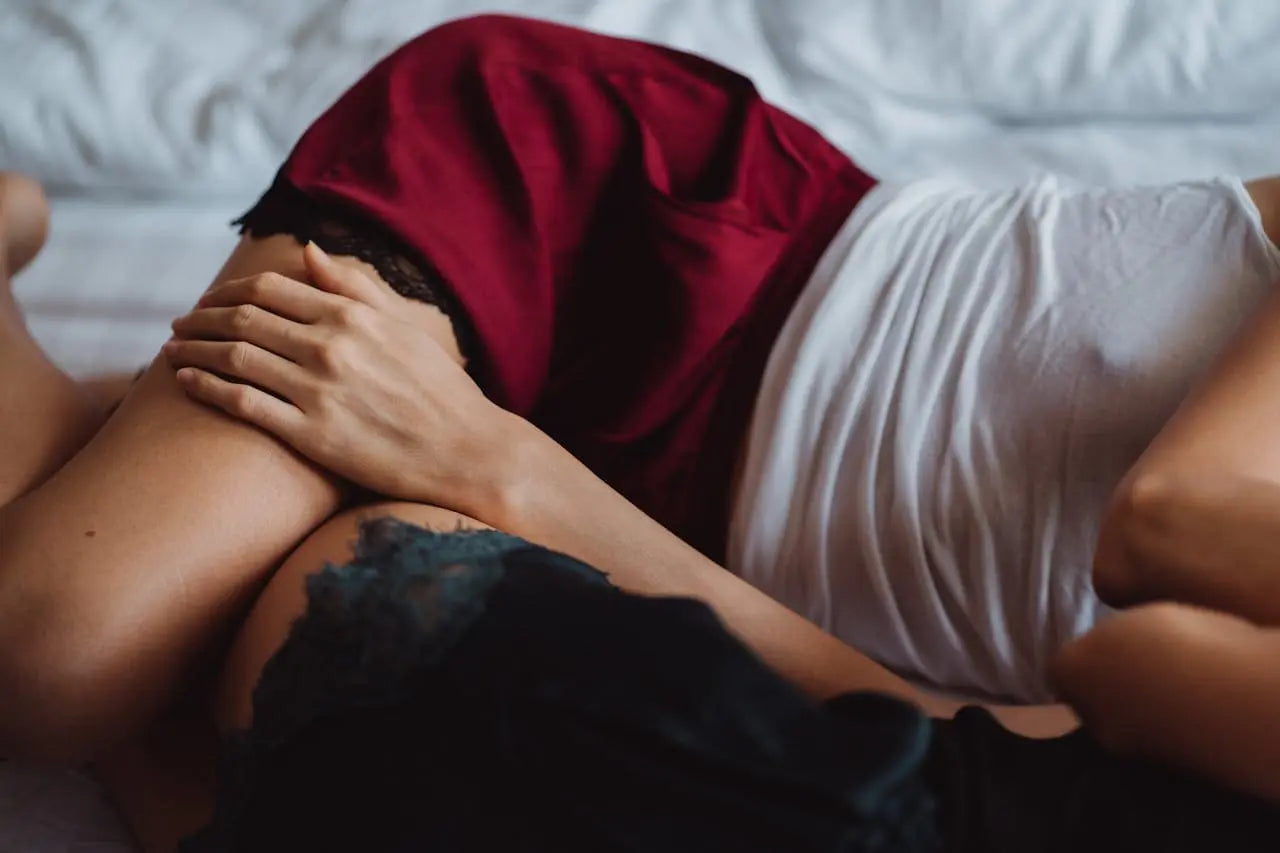 Deux partenaires allongé(e)s ensemble sur un lit, enlacé(e)s, illustrant une intimité partagée et une relation de confiance dans le couple.