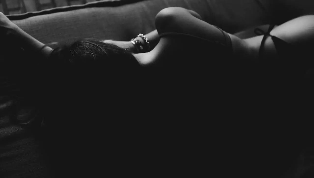 Femme allongée sur un canapé, photographiée en noir et blanc, dans une atmosphère feutrée et intime.